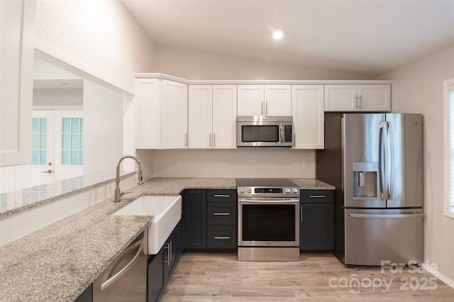kitchen with light stone countertops, white cabinets, a sink, vaulted ceiling, and stainless steel appliances
