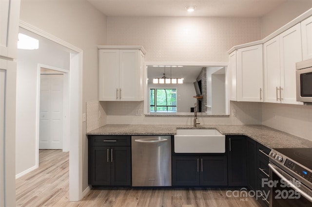 kitchen featuring light wood-type flooring, a sink, light stone counters, stainless steel appliances, and white cabinetry