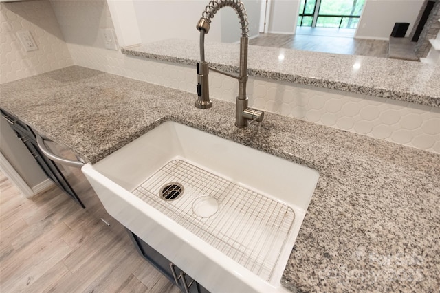 room details featuring light stone counters, a sink, decorative backsplash, and wood finished floors
