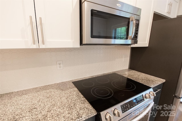 kitchen featuring appliances with stainless steel finishes, white cabinets, decorative backsplash, and light stone countertops