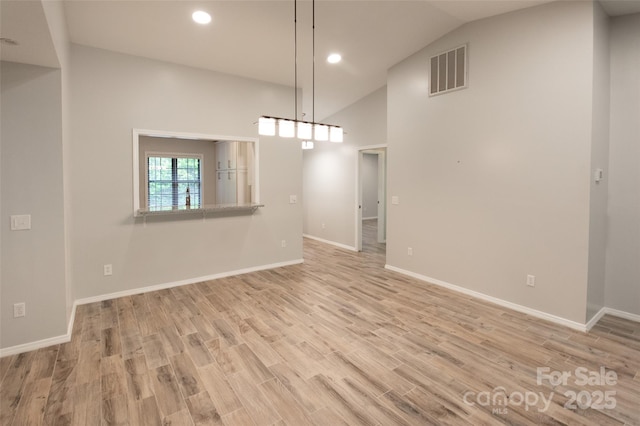 interior space featuring visible vents, light wood-style floors, baseboards, and vaulted ceiling