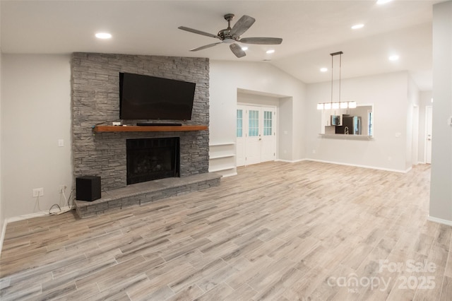 unfurnished living room featuring wood finished floors, lofted ceiling, a stone fireplace, baseboards, and ceiling fan