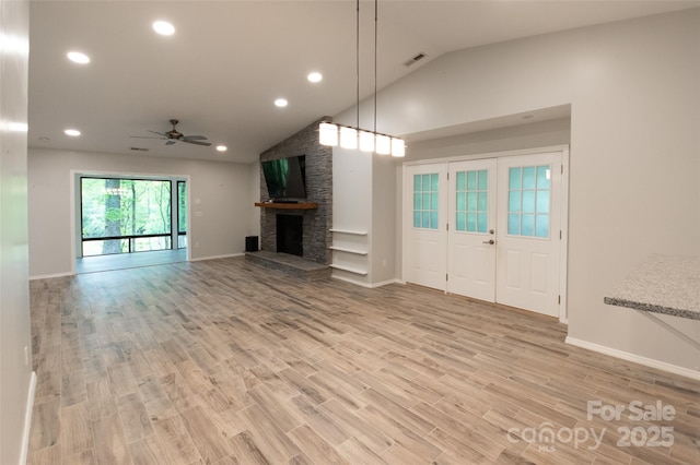 unfurnished living room with ceiling fan, a stone fireplace, visible vents, vaulted ceiling, and light wood-type flooring