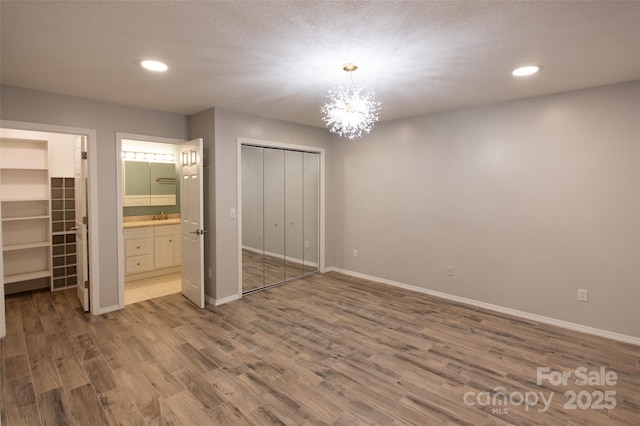 unfurnished bedroom featuring baseboards, a closet, wood finished floors, and a notable chandelier