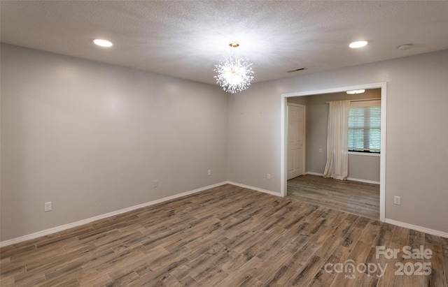 spare room featuring an inviting chandelier, visible vents, wood finished floors, baseboards, and recessed lighting
