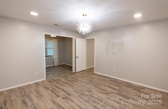 spare room featuring a notable chandelier, recessed lighting, baseboards, wood finished floors, and visible vents