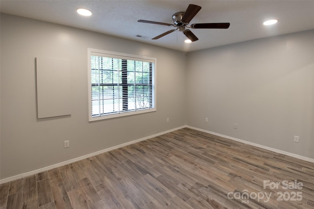 empty room with a ceiling fan, visible vents, wood finished floors, baseboards, and recessed lighting