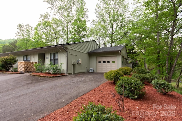 single story home with an attached garage, a chimney, and driveway