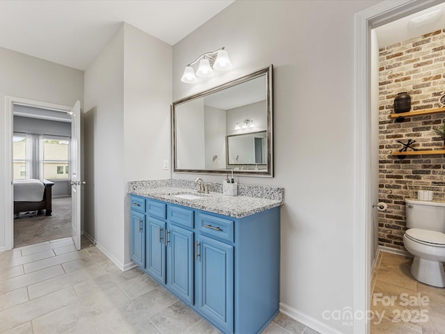 bathroom with brick wall, vanity, baseboards, toilet, and connected bathroom