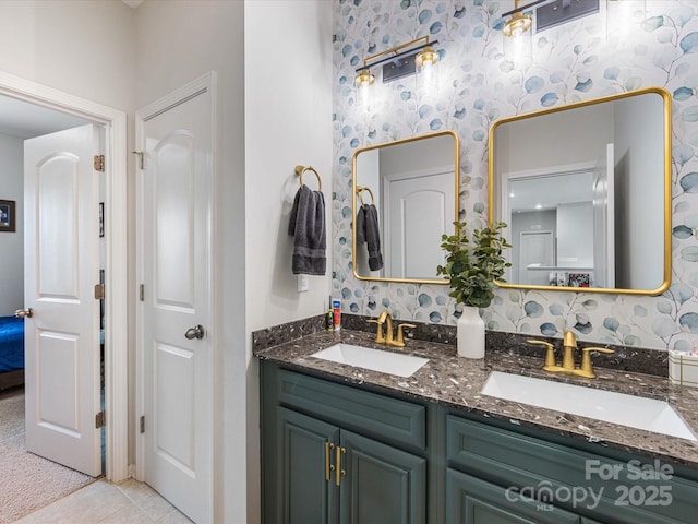 ensuite bathroom with a sink, tile patterned floors, wallpapered walls, and double vanity