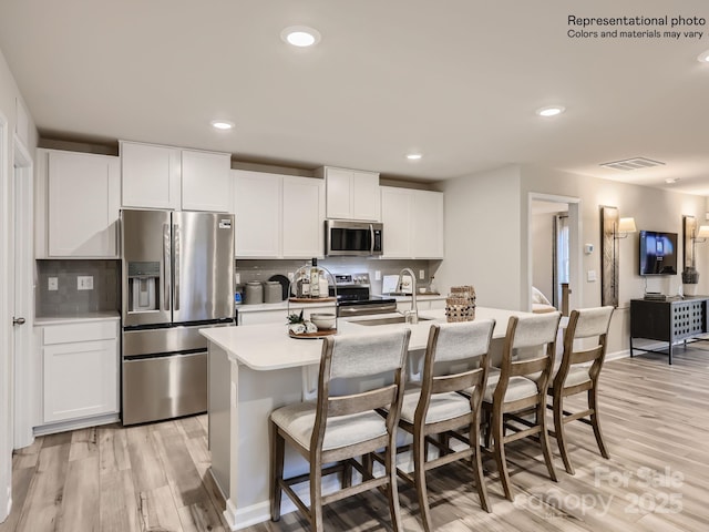 kitchen with appliances with stainless steel finishes, tasteful backsplash, and light wood-type flooring