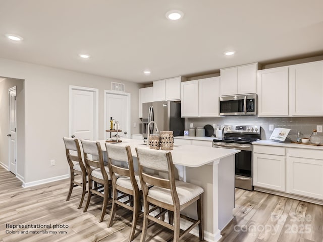 kitchen featuring visible vents, light countertops, stainless steel appliances, light wood-style flooring, and an island with sink