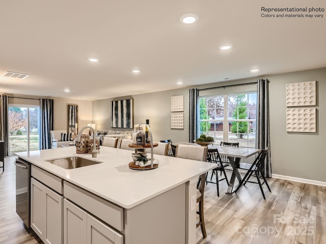 kitchen featuring open floor plan, an island with sink, light wood-type flooring, a sink, and dishwasher