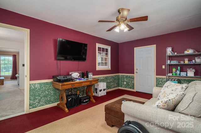 living room featuring carpet floors, baseboards, a wainscoted wall, and a ceiling fan