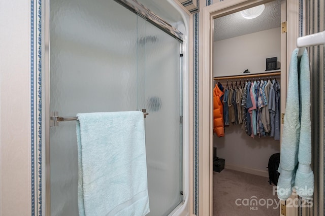full bathroom featuring baseboards, a textured ceiling, a shower stall, and a walk in closet