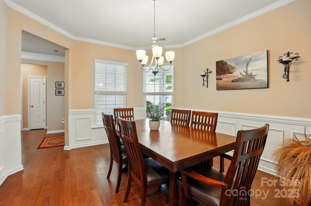 dining room featuring wainscoting, a decorative wall, a chandelier, wood finished floors, and ornamental molding