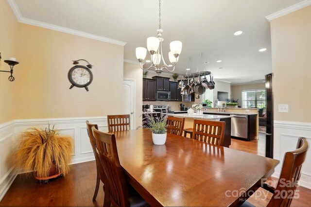 dining area featuring a wainscoted wall, ornamental molding, hardwood / wood-style floors, and a chandelier