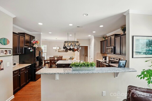 kitchen featuring decorative backsplash, light stone countertops, dark brown cabinets, a peninsula, and stainless steel appliances