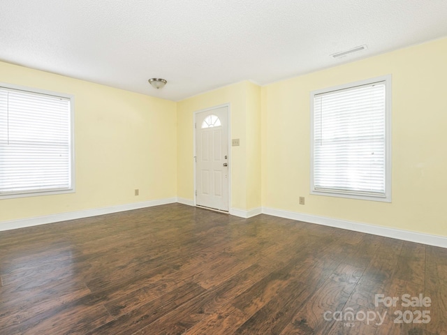 unfurnished living room with baseboards, a textured ceiling, dark wood-style floors, and visible vents