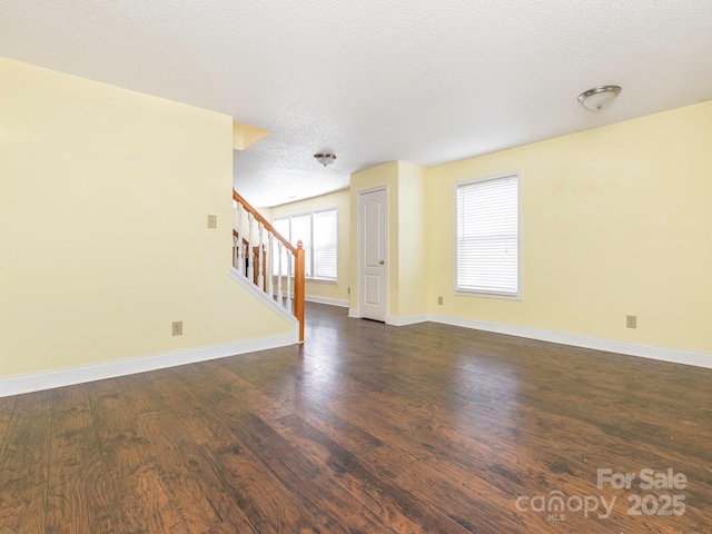 empty room featuring baseboards, a textured ceiling, dark wood-style floors, and stairway