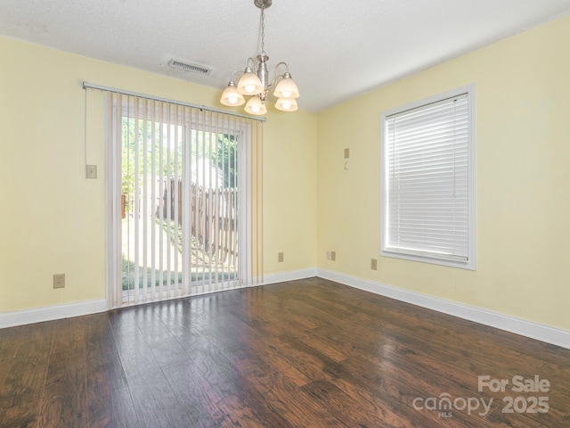 spare room with baseboards, a notable chandelier, wood finished floors, and visible vents