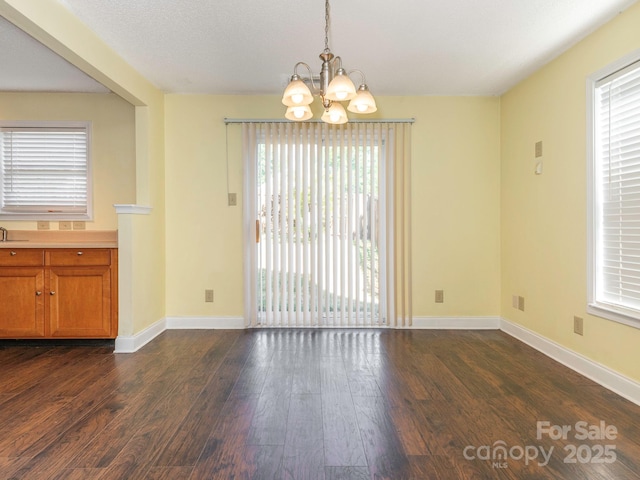 unfurnished dining area featuring an inviting chandelier, baseboards, and dark wood-style flooring