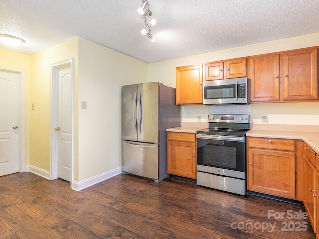 kitchen featuring brown cabinetry, dark wood-style flooring, light countertops, a textured ceiling, and stainless steel appliances