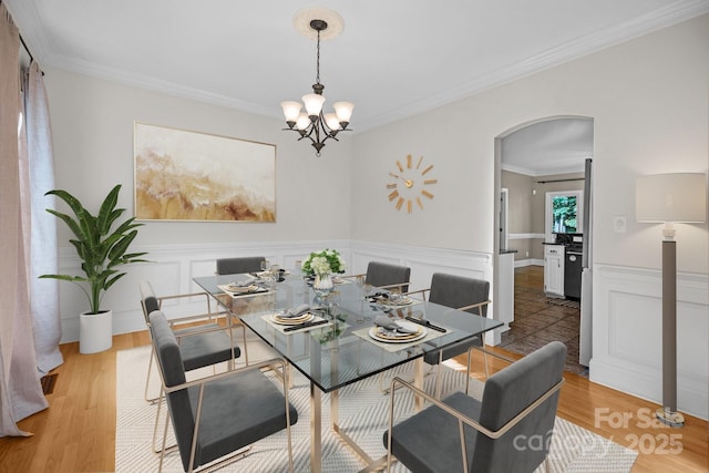 2608 Carmarthen Ct, Matthews, NC 28104 - dining space featuring arched walkways, a chandelier, wood finished floors, crown molding, and a wainscoted wall