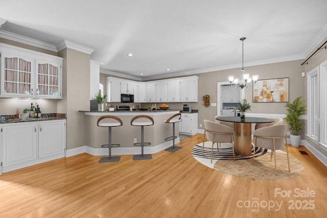2608 Carmarthen Ct, Matthews, NC 28104 - kitchen featuring black microwave, light wood-style flooring, dark countertops, white cabinets, and a chandelier