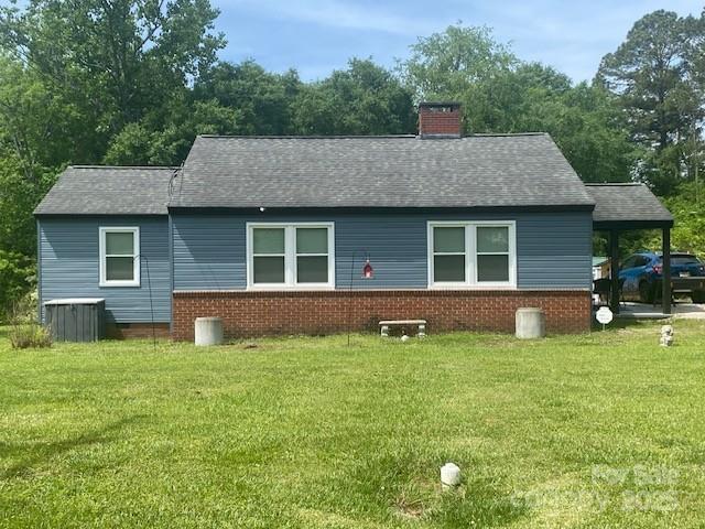 view of front of house with brick siding, a chimney, a shingled roof, and a front lawn