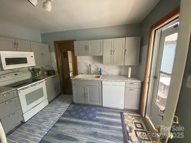 kitchen featuring a sink, dark wood finished floors, white appliances, and light countertops