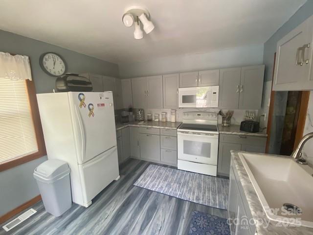kitchen with a sink, gray cabinets, white appliances, and visible vents