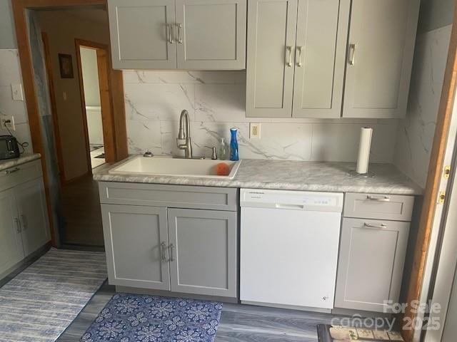kitchen with light countertops, dark wood-style flooring, a sink, and dishwasher