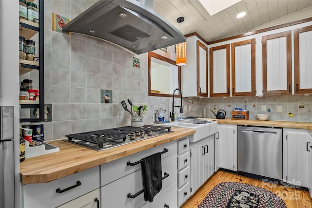 kitchen with exhaust hood, backsplash, appliances with stainless steel finishes, and butcher block counters