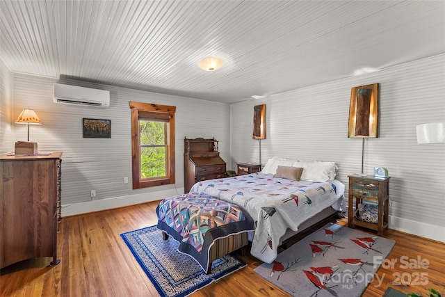 bedroom with baseboards, a wall mounted air conditioner, and wood finished floors