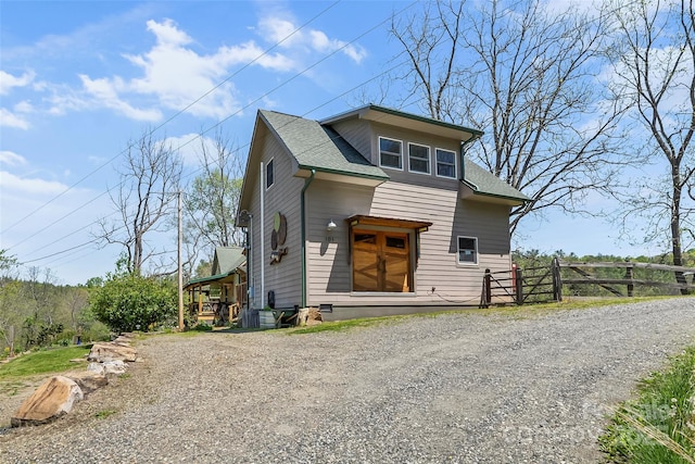 view of front of house with fence, roof with shingles, and gravel driveway