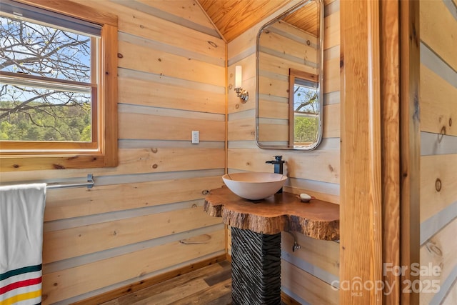 bathroom with a sink, wood ceiling, vaulted ceiling, and wooden walls