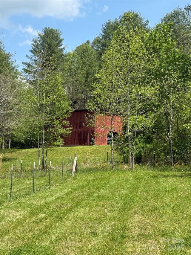 view of yard featuring fence, a wooded view, and an outdoor structure