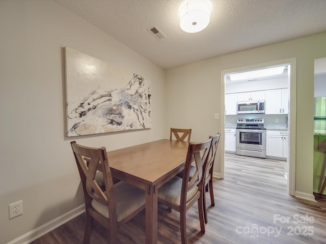 dining area with a textured ceiling, visible vents, baseboards, and light wood-style floors