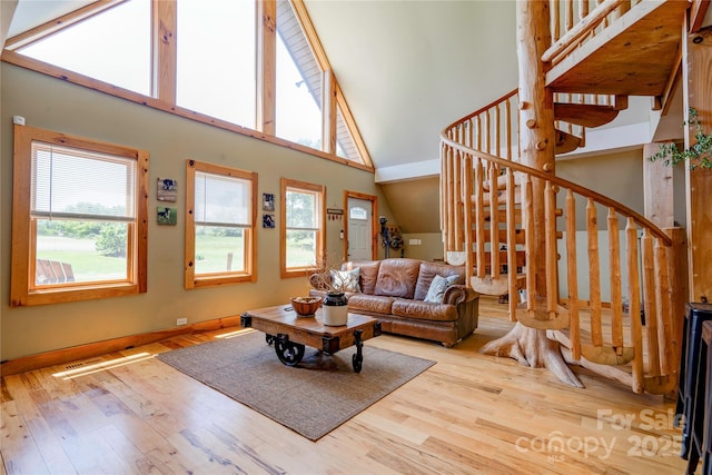 living area with baseboards, high vaulted ceiling, wood finished floors, and stairway
