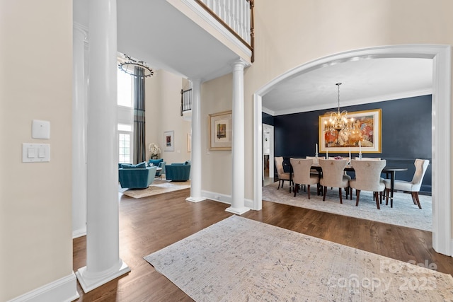 foyer with a towering ceiling, arched walkways, a chandelier, ornate columns, and dark wood-type flooring