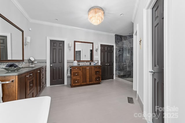 bathroom featuring crown molding, two vanities, a stall shower, and a notable chandelier