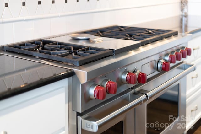 room details featuring dark countertops, tasteful backsplash, double oven range, and white cabinets