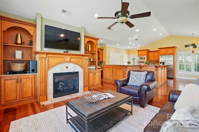 living room with visible vents, lofted ceiling, a tile fireplace, a ceiling fan, and light wood-style flooring