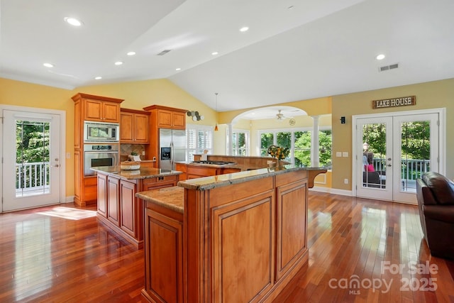 kitchen with brown cabinets, stainless steel appliances, a large island, ornate columns, and visible vents