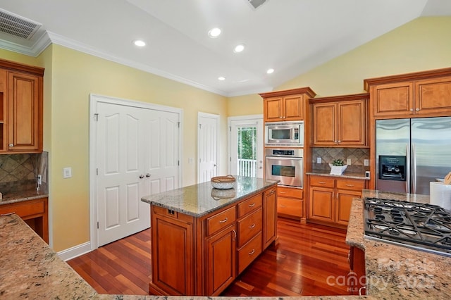 kitchen with brown cabinetry, light stone counters, ornamental molding, stainless steel appliances, and dark wood-type flooring