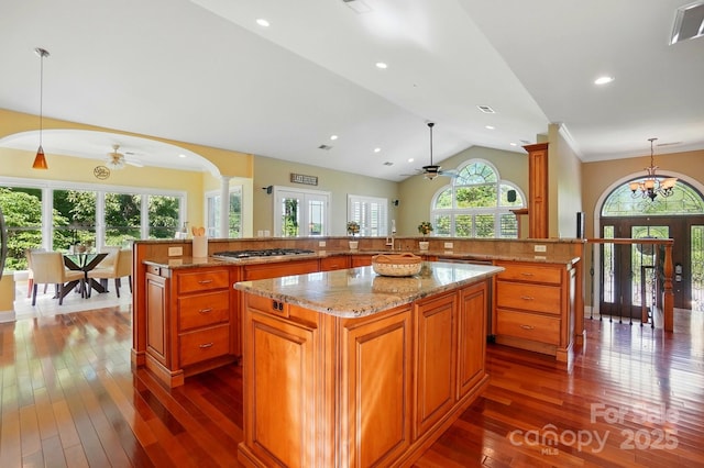 kitchen with ceiling fan, stainless steel gas cooktop, dark wood finished floors, brown cabinetry, and a large island