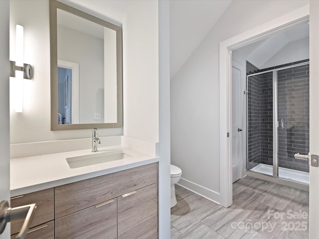 bathroom with vanity, toilet, baseboards, a shower stall, and vaulted ceiling