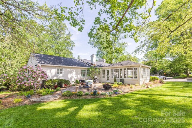 rear view of house featuring a chimney, a sunroom, a yard, a patio, and a fire pit