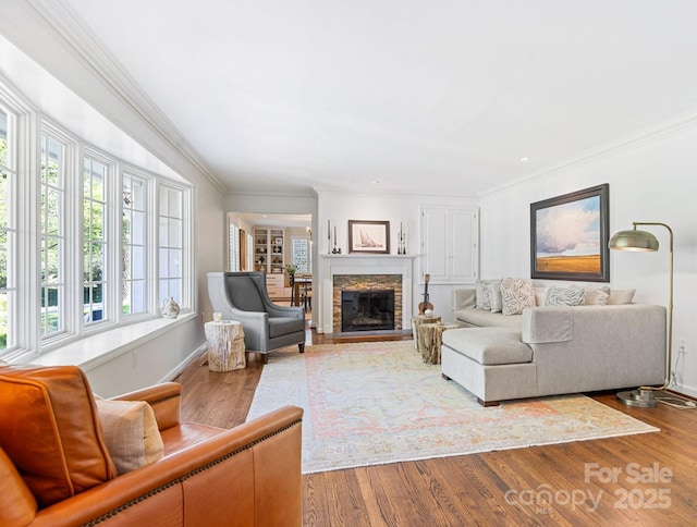 living area with baseboards, a stone fireplace, ornamental molding, and wood finished floors